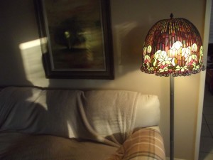White leather sofa covered with blankets, lighted by a Tiffany Lamp reproduction.