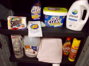 A variety of household cleaners and laundry products, stored in a plastic cabinet in a garage.